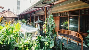 A covered outdoor area with a wooden bench, potted plants, and a tiled floor. - Tempo Doeloe Homestay (Kuta)