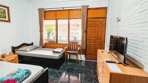 A bedroom with a bed, a desk with a computer, a TV, and a window with curtains. - Tempo Doeloe Homestay (Kuta)