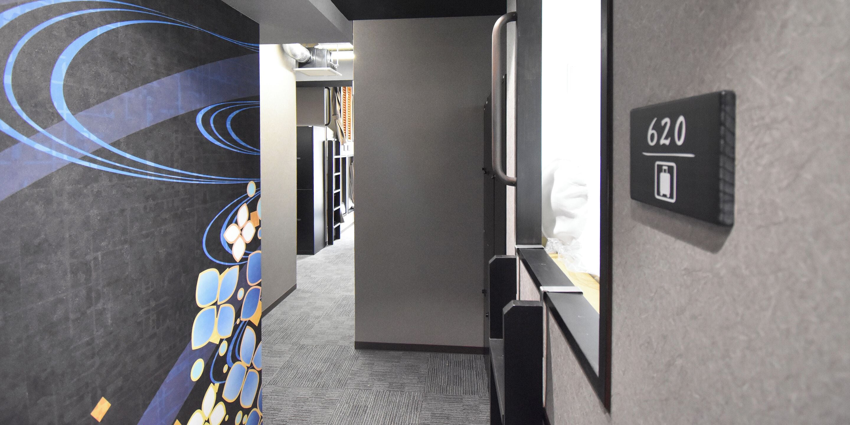 Un couloir au design moderne, avec un mur orné d’un motif géométrique et une signalétique indiquant le numéro de la chambre : 620.