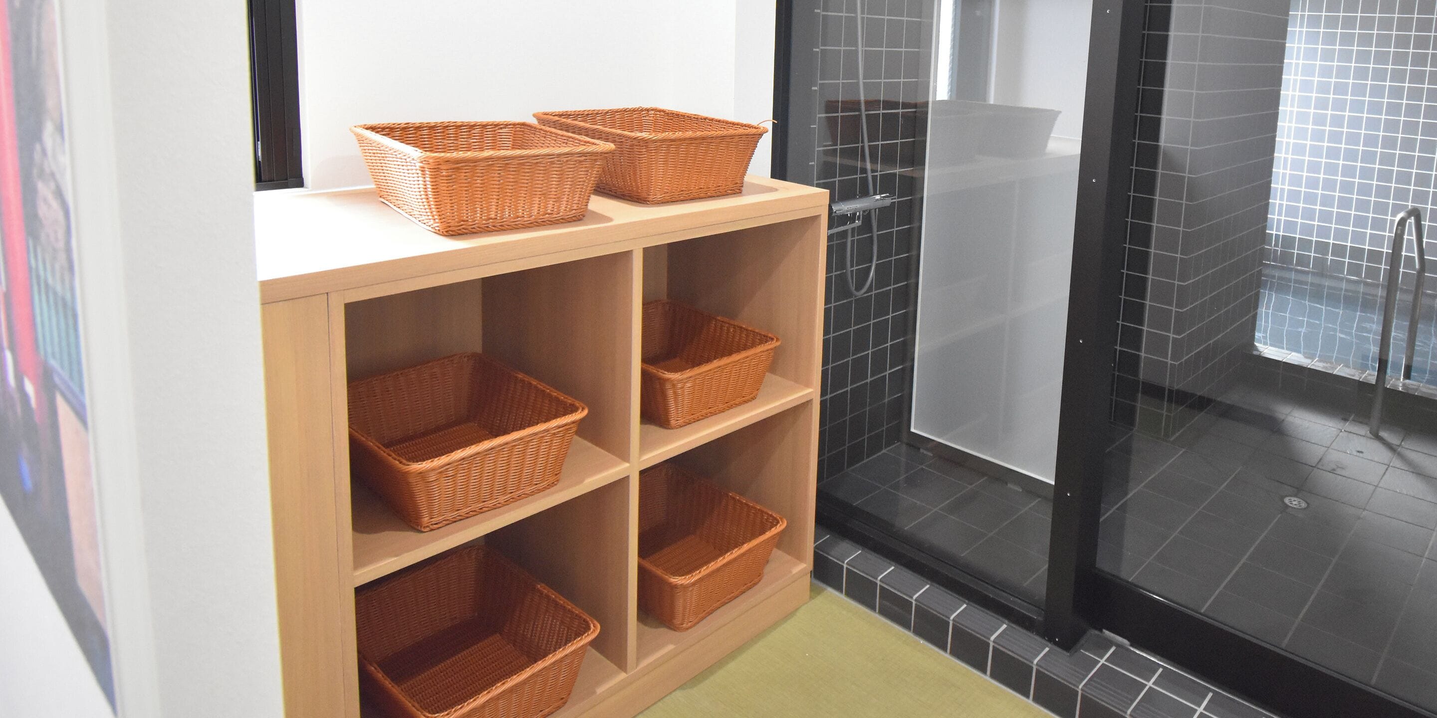 Ein Badezimmer mit einem Holzboden, Körben aus Weidwerk, einer Duschkabine aus Glas und schwarzen Fliesen.