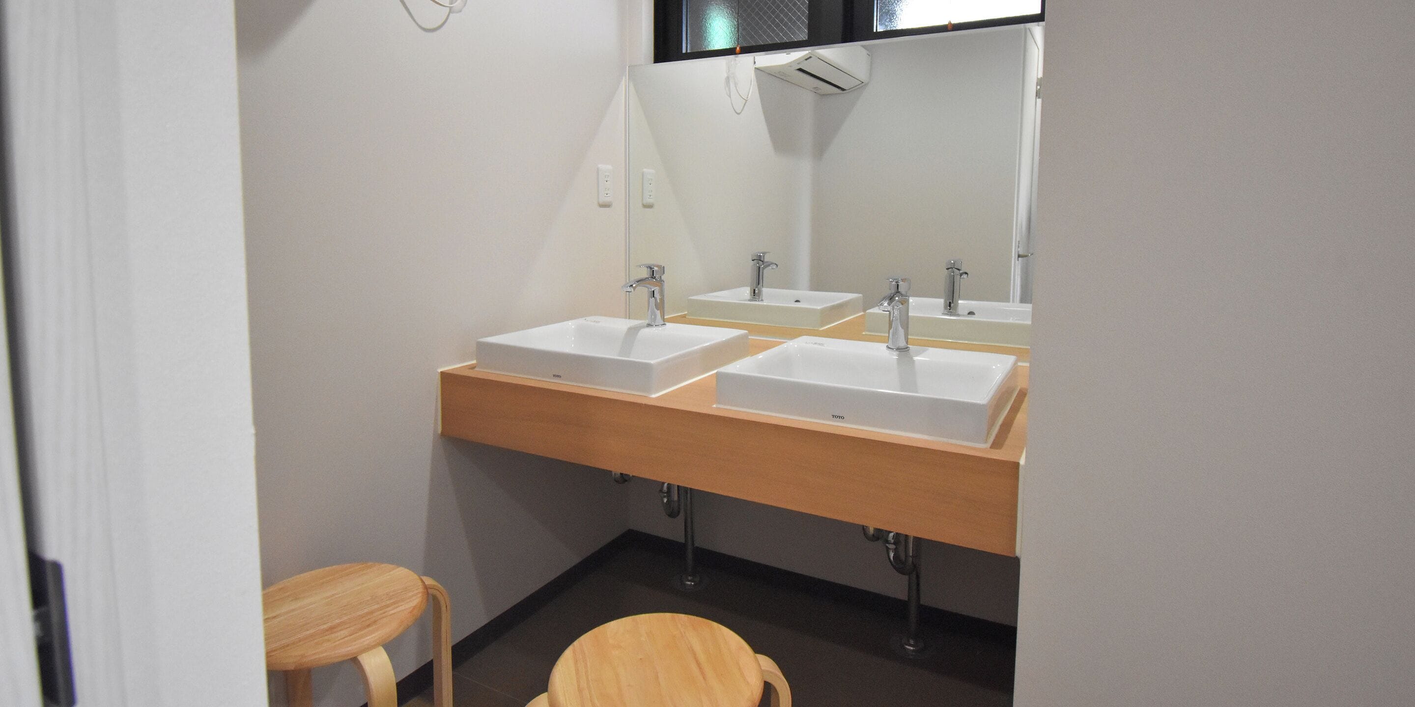 A bathroom with three sinks, a mirror, and a wooden stool.