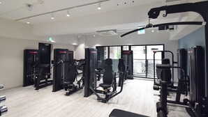 Un gimnasio con diferentes máquinas de ejercicio, una banca y una puerta que da al exterior.