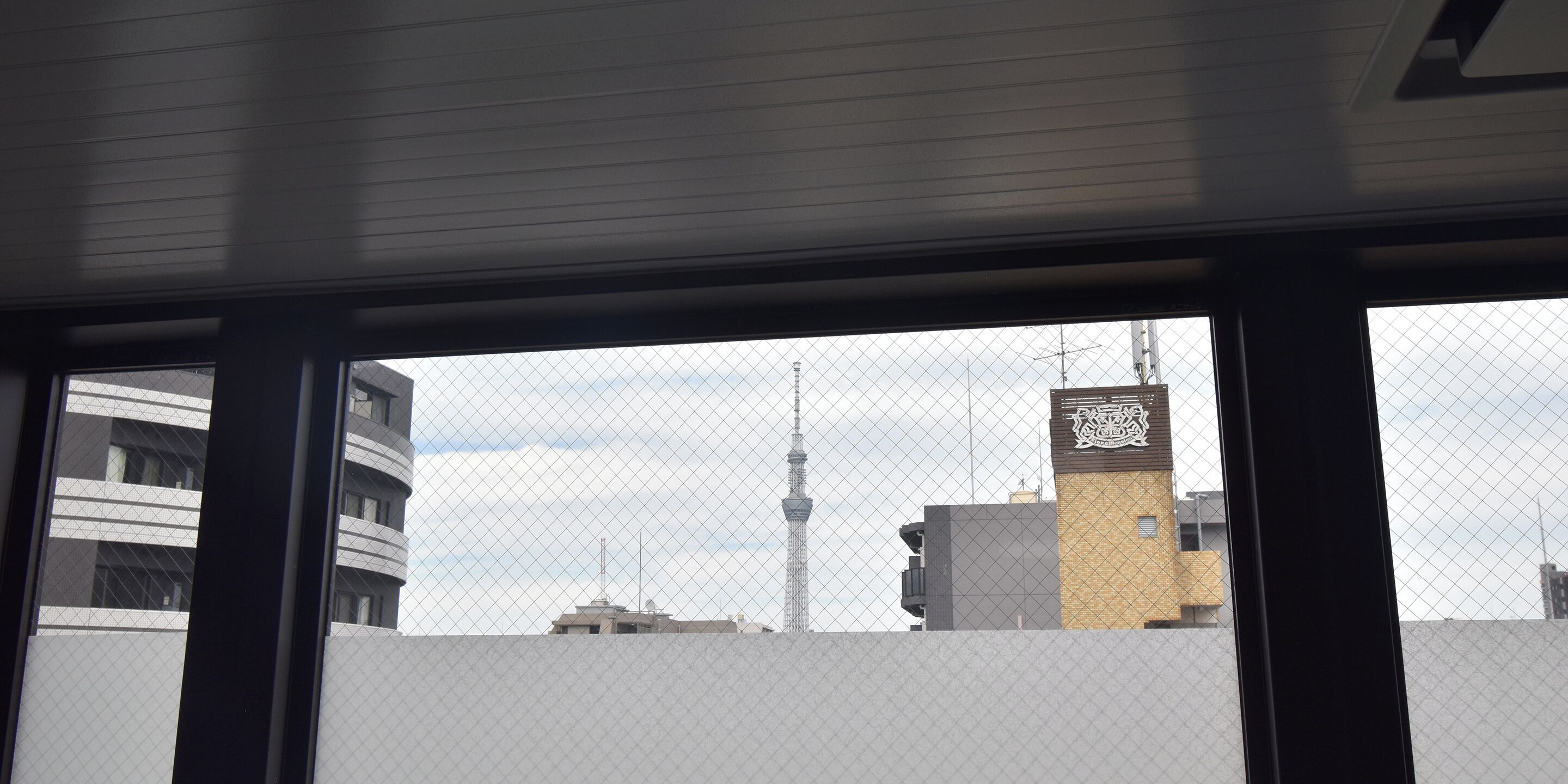 A view through a window with a metal fence, featuring a tower and several buildings.