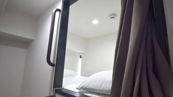 Una habitación de hotel con cama, ventana con cortinas, una lámpara en el techo y un enchufe de pared.