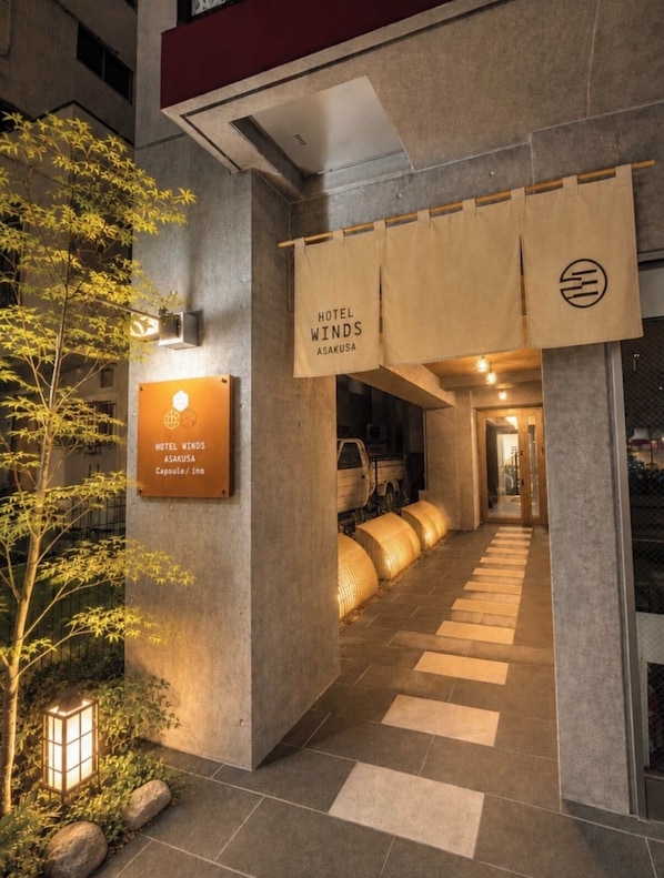 A hotel entrance with a sign for Hotel Winds Asakusa, a capsule inn, and a pathway leading inside.