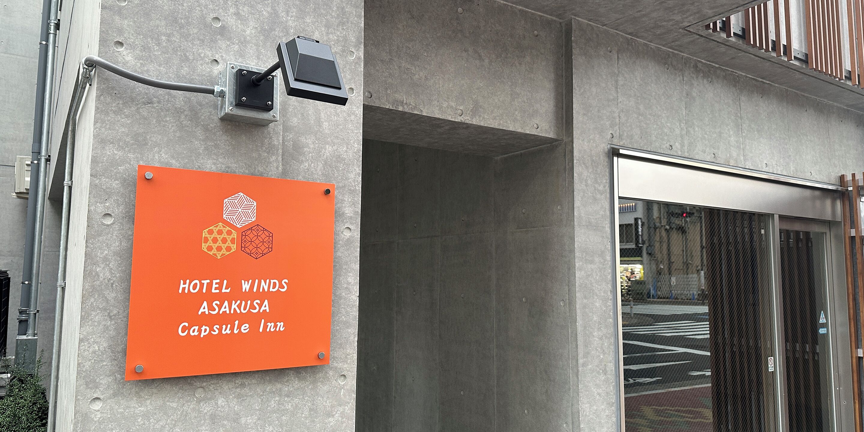 A sign for Hotel Winds Asakusa Capsule Inn on a concrete wall.