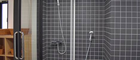 Douchecabine met betegelde wand, handdouche en douchekop aan de muur.