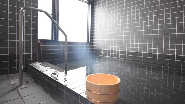 Una sauna con paredes de azulejos negros, un banco de madera y una barandilla de metal.