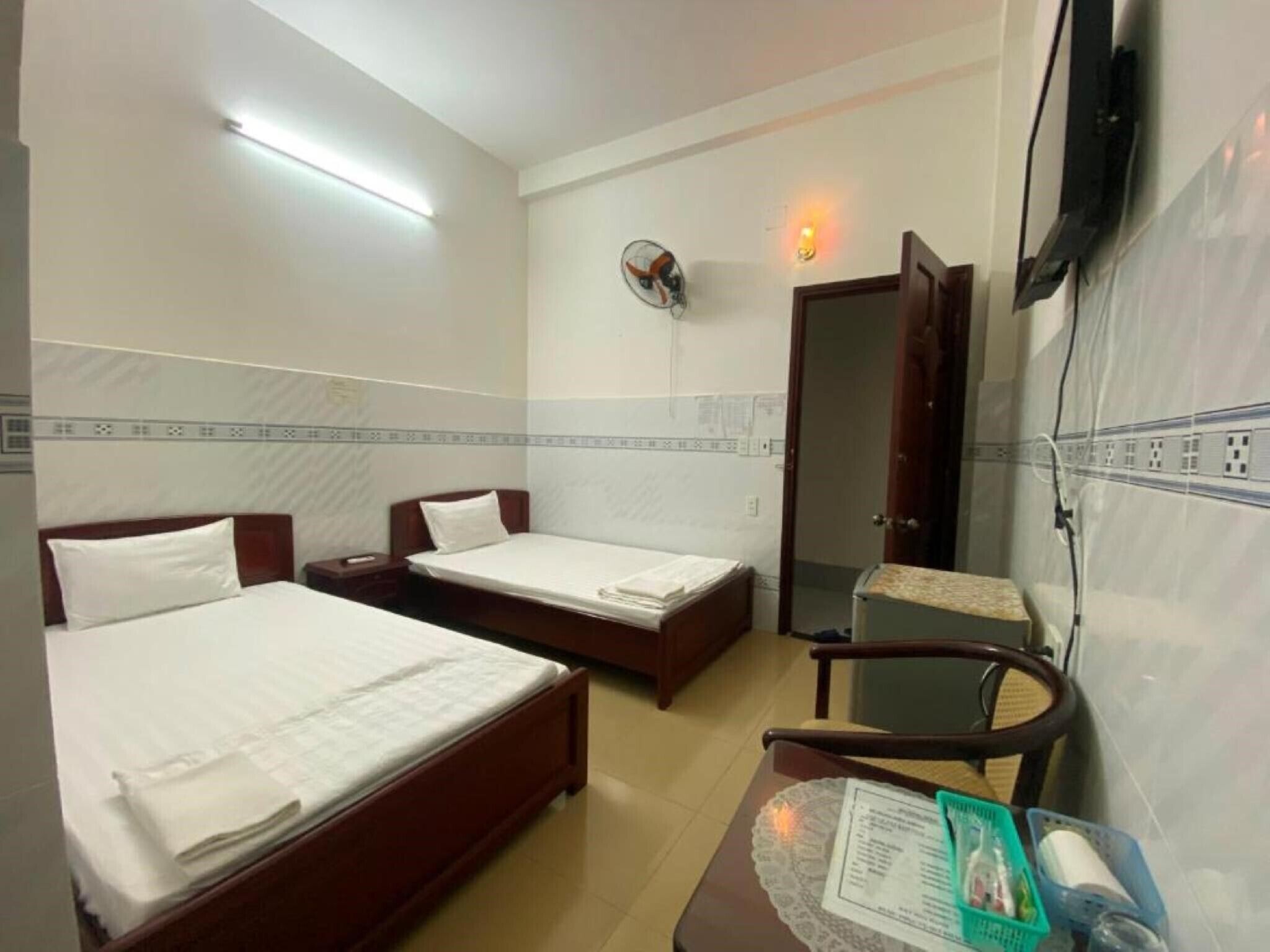 Habitación de hotel con dos camas, una mesa pequeña con un menú, una silla, televisor montado en la pared y una puerta.