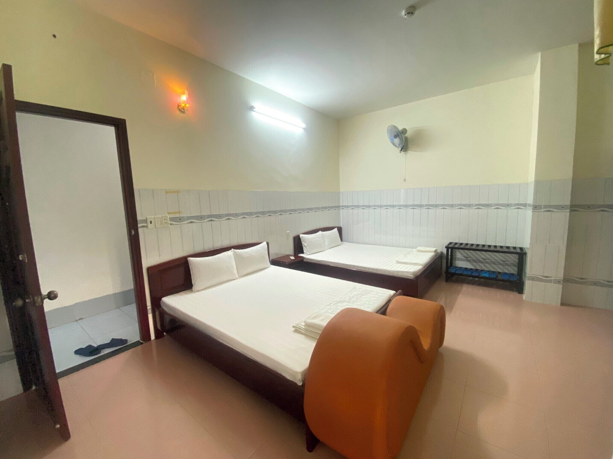 Ein Hotelzimmer mit zwei Einzelbetten, einem kleinen orangefarbenen Sessel, einem Nachttisch und einem an der Wand befestigten Heizkörper.
