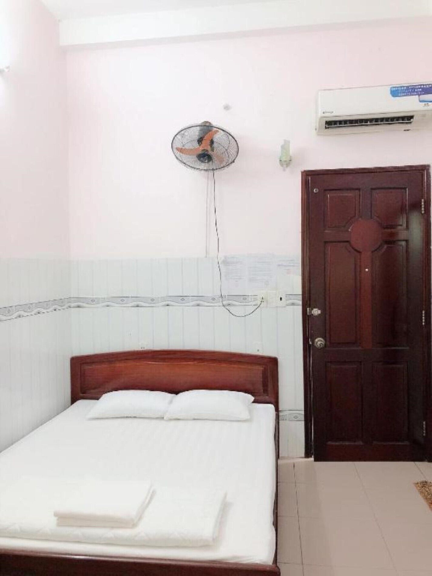 Un dormitorio con cama de madera, un ventilador de pared y un equipo de aire acondicionado.
