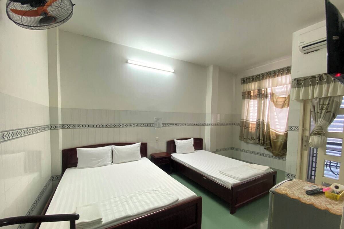 Una habitación de hotel con dos camas individuales, una mesita, un ventilador y una ventana con cortinas.