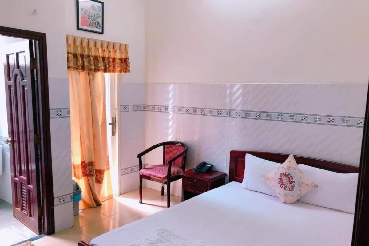 Una habitación de hotel con una cama, una silla, una mesita de noche y una cortina.