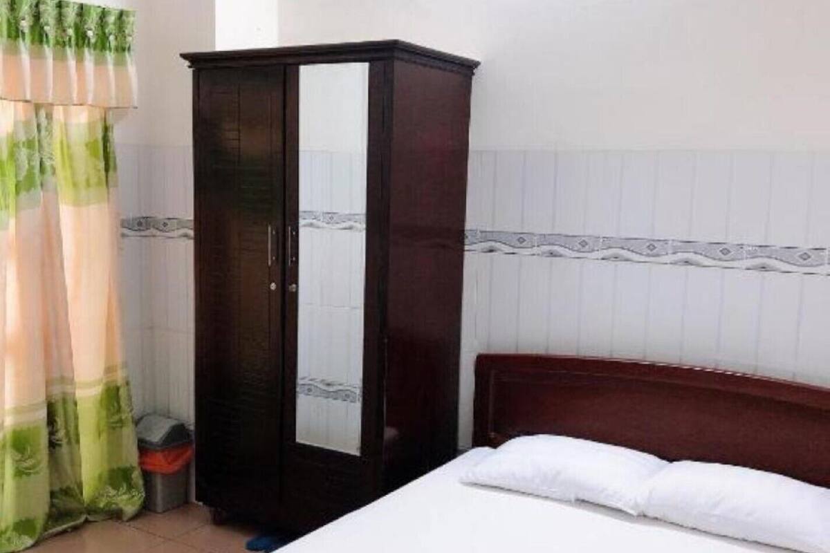 Una cama bien hecha con sábanas blancas, un armario de madera oscura y una cortina verde y blanca.