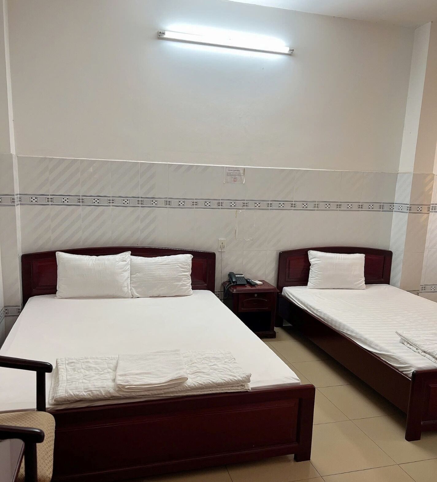 A hotel room with two beds, a bedside table with a phone, and a wall-mounted light fixture.