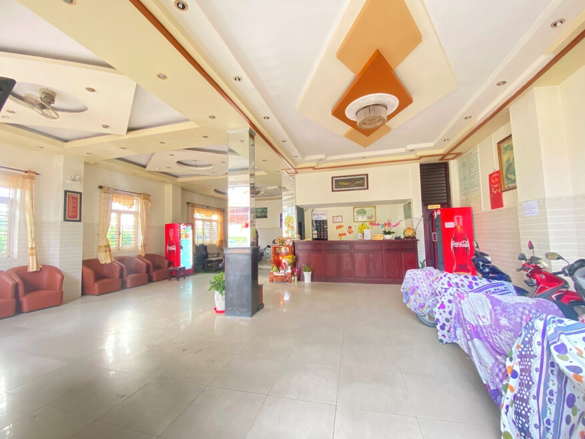 A hotel lobby with a reception desk, seating area, and a Coca-Cola refrigerator.