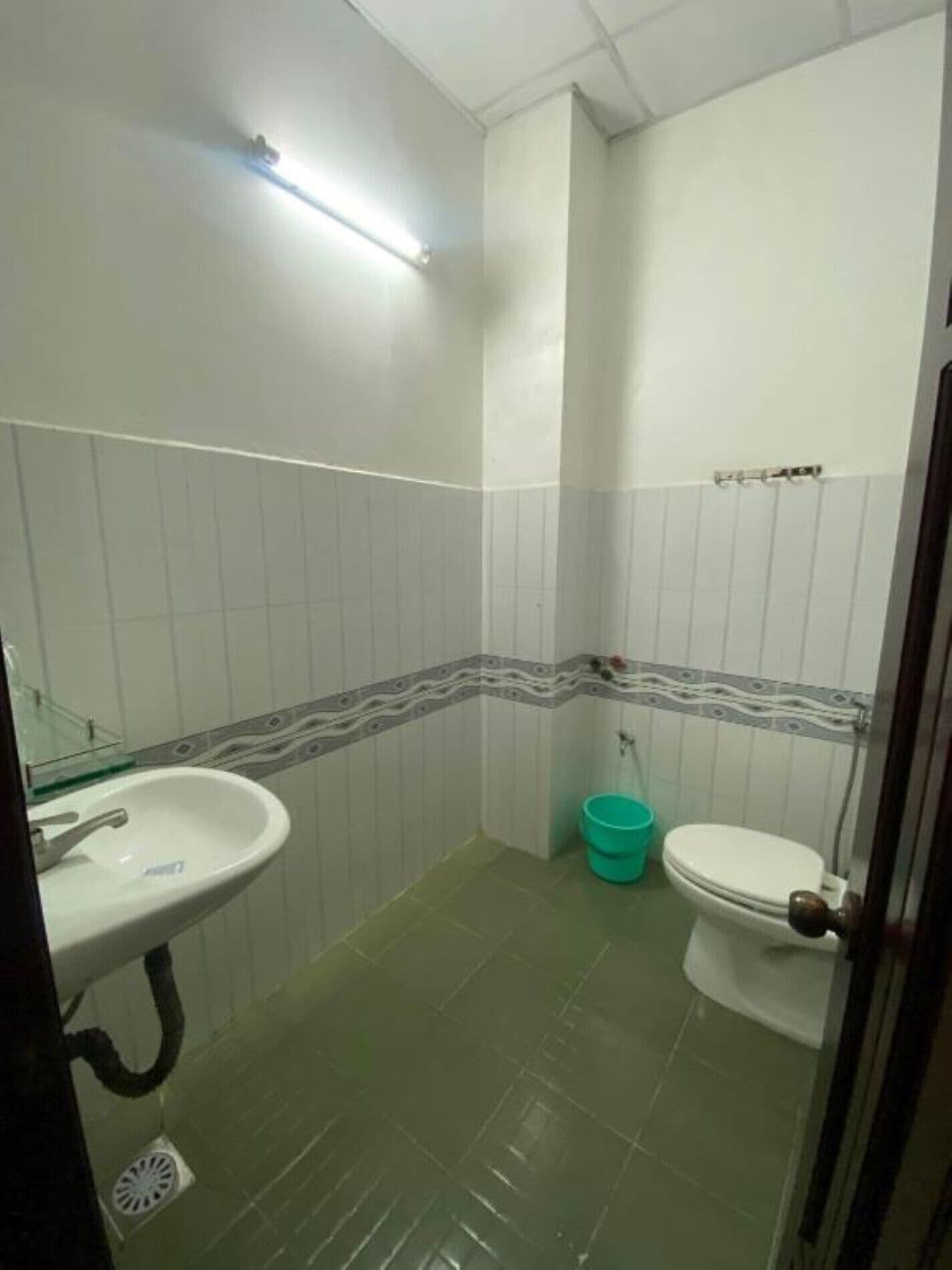 A small, basic bathroom with a sink, toilet, and a green bucket.