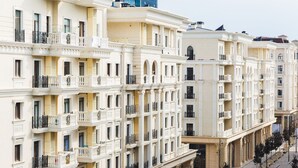 A row of multi-story buildings with balconies, large windows, and a clear sky.