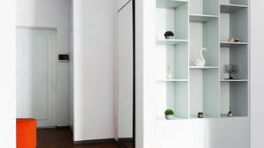A modern interior with a white door, a black-framed mirror, and a white shelving unit with decorative items.