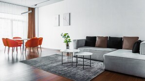A modern living room with a grey sofa, orange chairs, a small white table, and a grey rug.