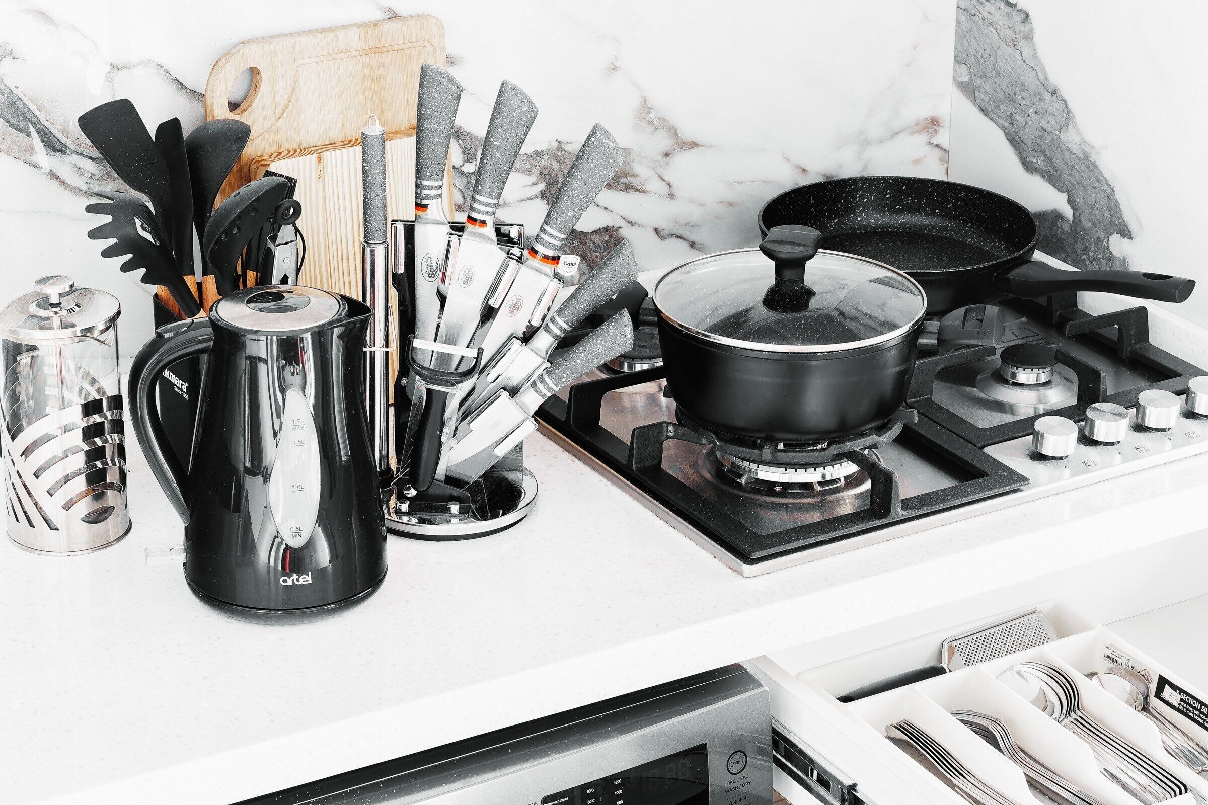 A kitchen with a stove, pots, utensils, and a coffee maker.
