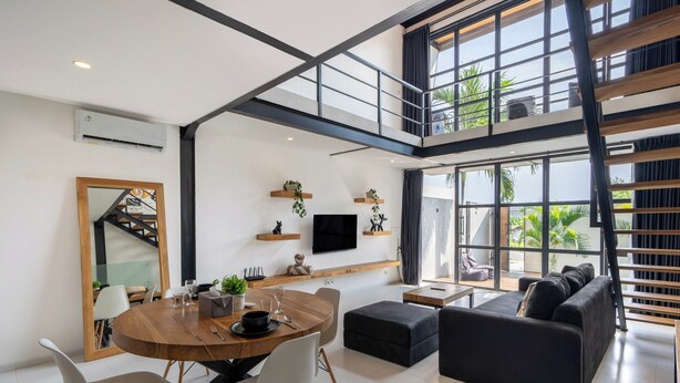 Un vaste espace de vie comprenant une table à manger, un canapé noir et un escalier menant à un niveau supérieur.