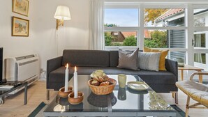Una sala de estar acogedora con un sofá gris, una mesa de centro de vidrio y vistas al exterior.