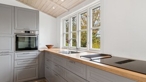 Una cocina moderna con armarios grises, horno empotrado, amplio ventanal con vista a árboles y encimera de madera.
