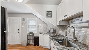 A kitchen with white cabinets, a marble countertop, a sink, and a sign that says 'Eat drink and be thankful.'