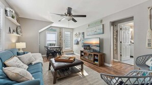 A living room with a blue sofa, a wooden coffee table, a ceiling fan, and a TV on a wooden stand.