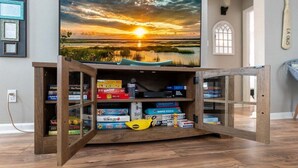 A room with a wooden entertainment center, a television displaying a sunset, and a window with a view of a building.