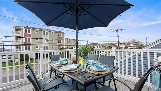 A balcony with a table set for dining, surrounded by chairs, and an umbrella providing shade.