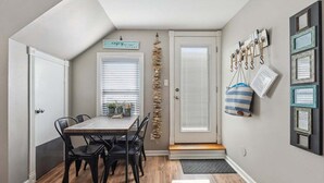 A dining area with a wooden table and chairs, a door with a doormat, and wall-mounted hooks with bags.