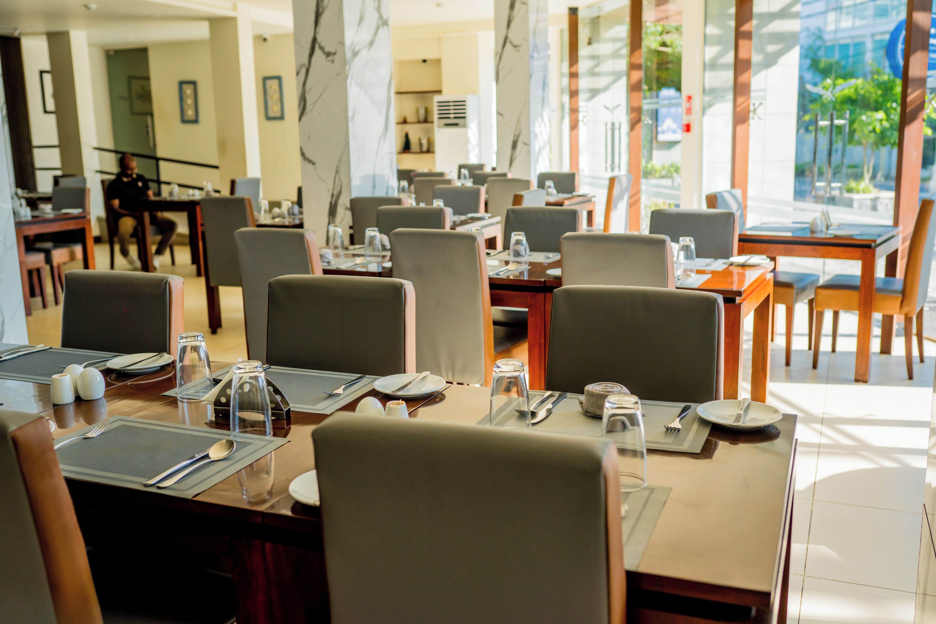 A hotel dining area with multiple tables set for guests, equipped with cutlery and glasses.