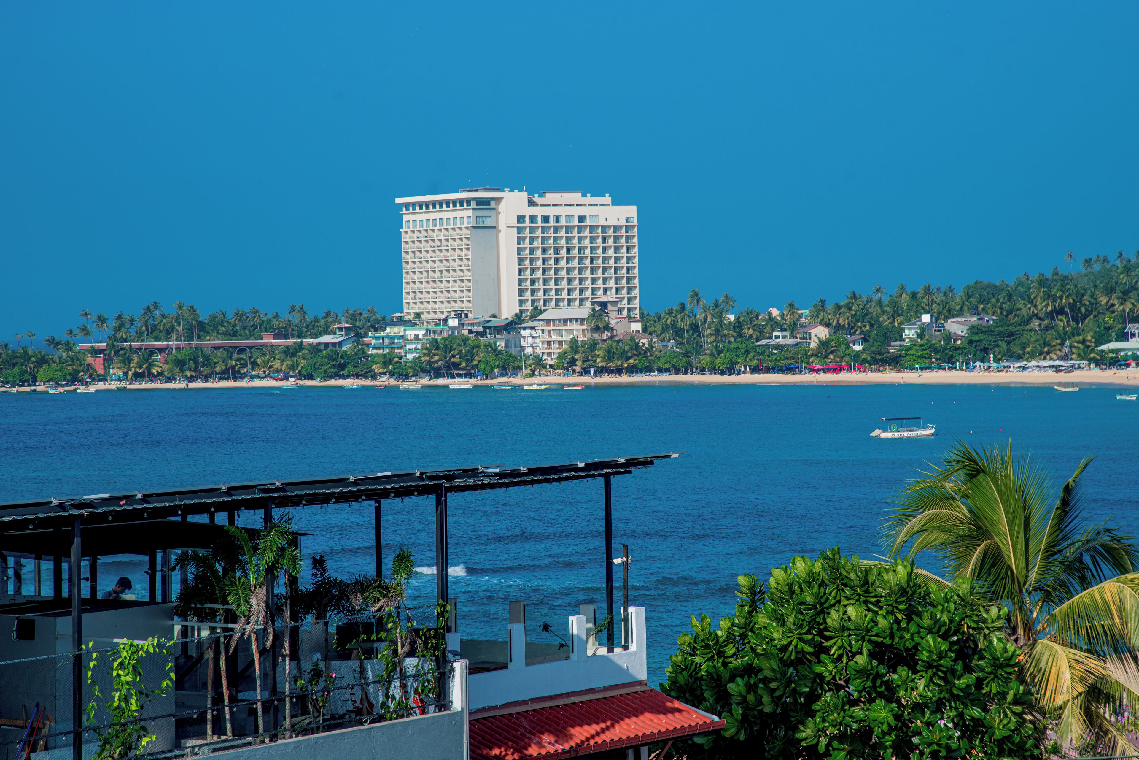 A coastal hotel with a view of the sea and a tall building in the background.