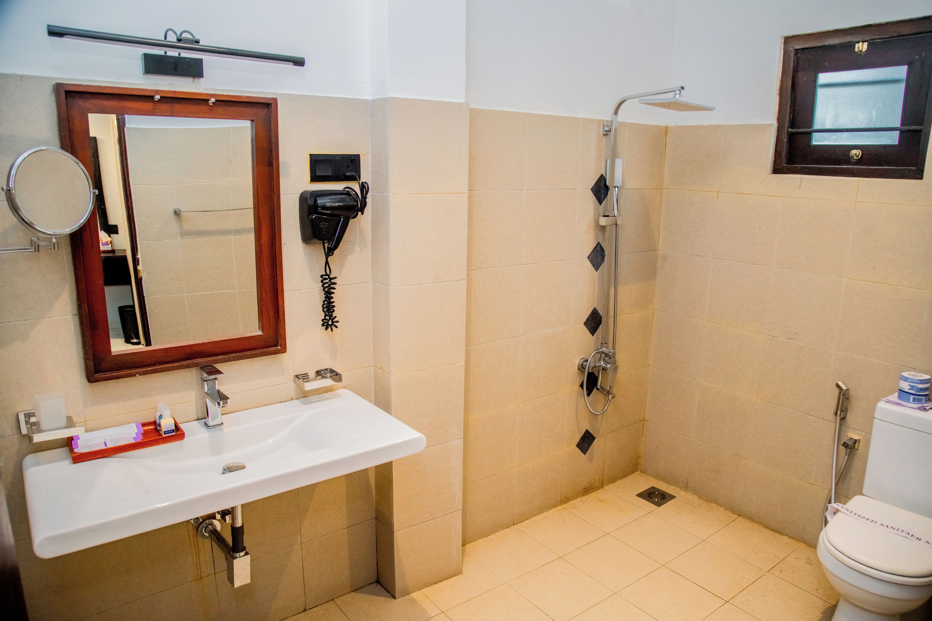 A bathroom with a sink, mirror, hairdryer, and shower.