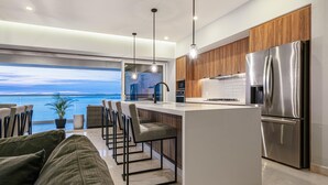 Una cocina moderna con una isla central, taburetes de bar y vistas al océano.
