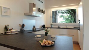 Una cocina moderna con una isla central, muebles de cocina blancos y una ventana con vistas a árboles.