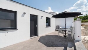 Un edificio moderno con un patio que incluye una mesa y sillas bajo un paraguas negro, una puerta y ventanas.