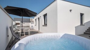 Un área de piscina moderna al aire libre, con un jacuzzi, una mesa y sillas, y una sombrilla grande.