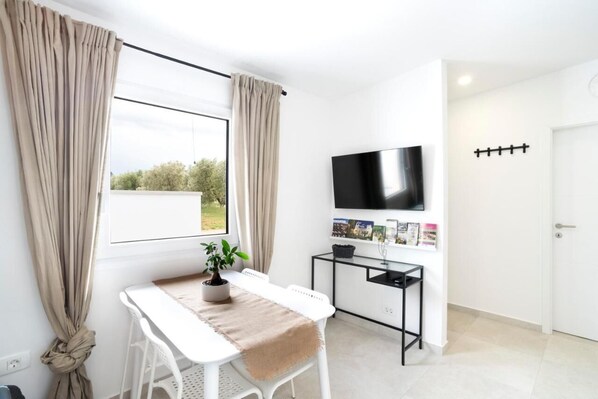 A modern room with a white table, a potted plant, a TV mounted on the wall, and a door with a handle.