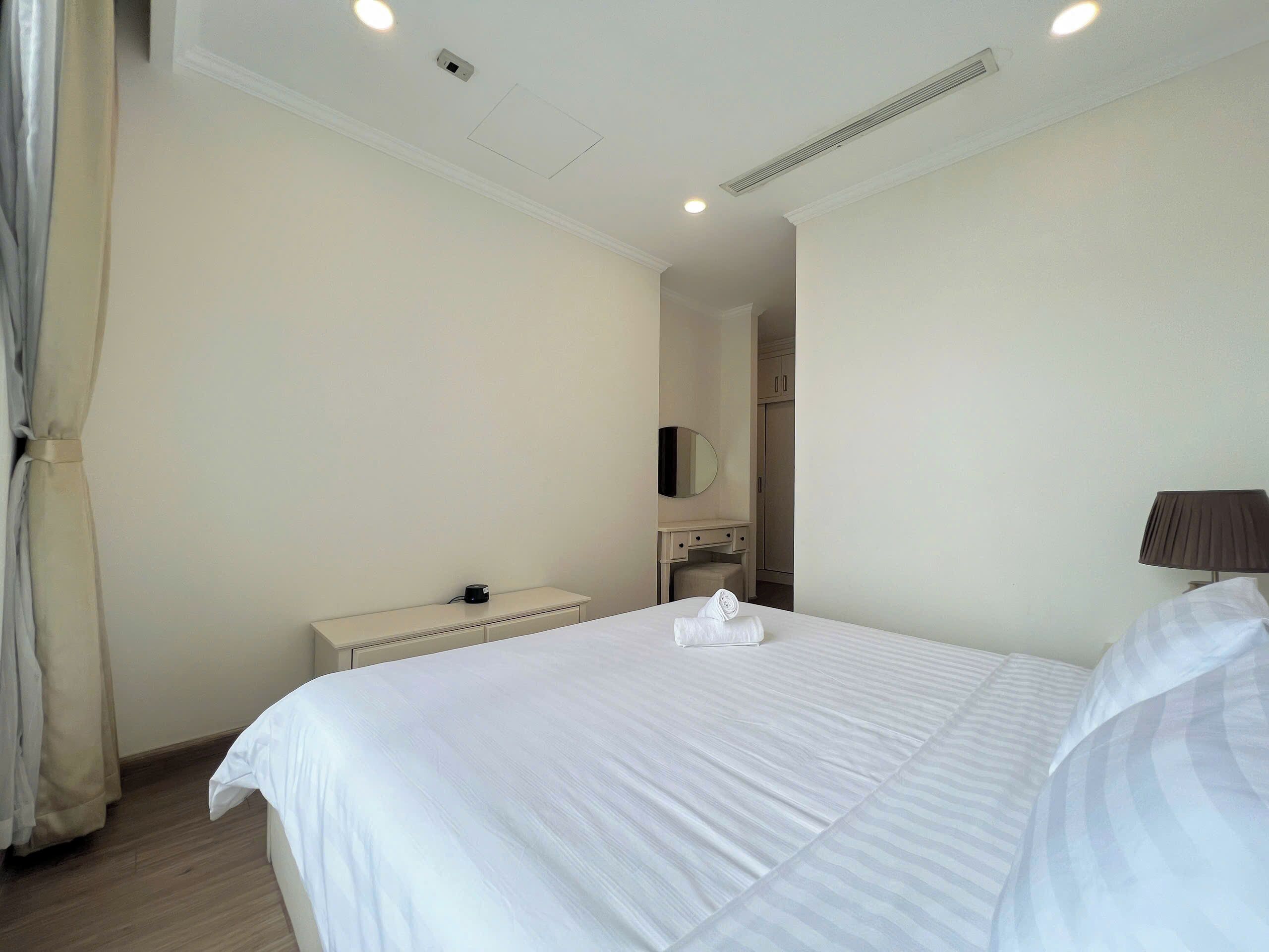 A hotel room with a large bed, a bedside table, a lamp, a mirror, and a wardrobe.