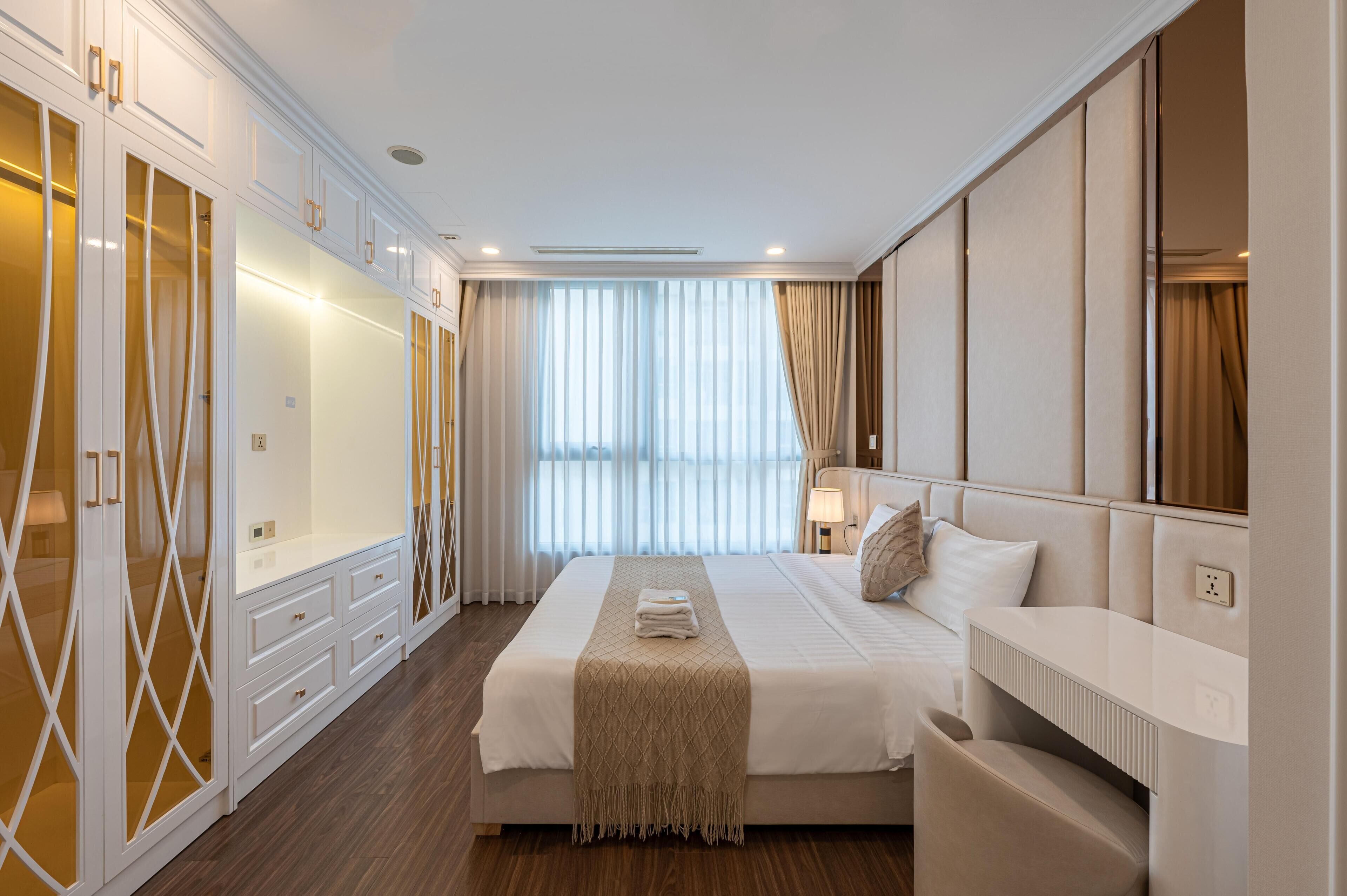 A hotel room with a large bed, a wardrobe, a bedside table, and a window with curtains.