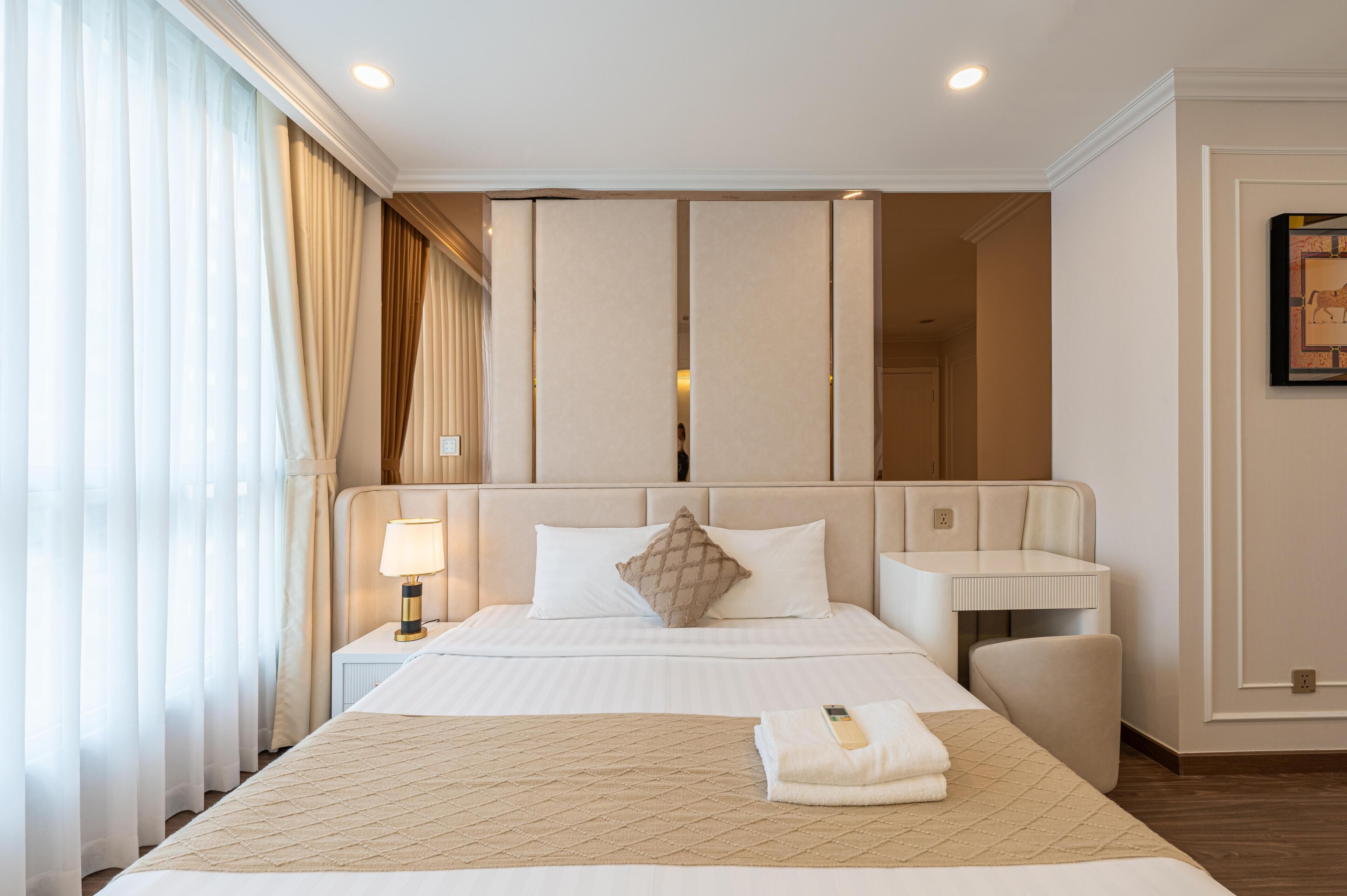 A hotel room with a large bed, a bedside table with a lamp, a small desk, and a mirror.