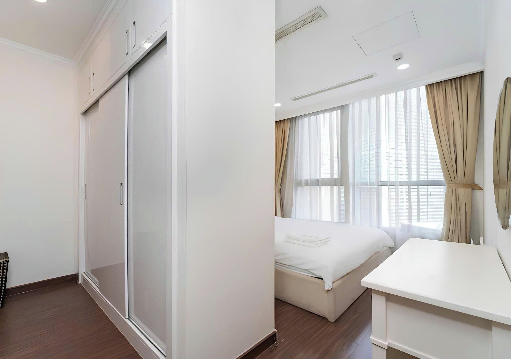 Une chambre d’hôtel équipée d’un lit, d’un bureau, d’une armoire et de grandes fenêtres avec des rideaux.
