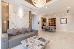 Un salon moderne avec un mur en marbre, un canapé gris, une table basse en marbre et un lustre.