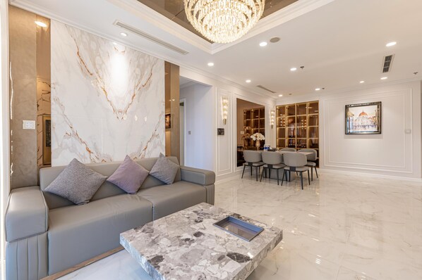 A modern living room with a marble wall, a grey sofa, a marble coffee table, and a chandelier.