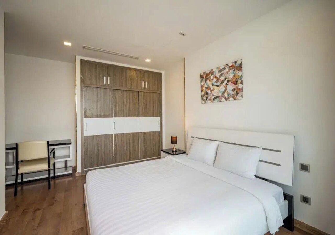 A bedroom with a bed, a desk, a chair, a wardrobe, and a wall-mounted artwork.