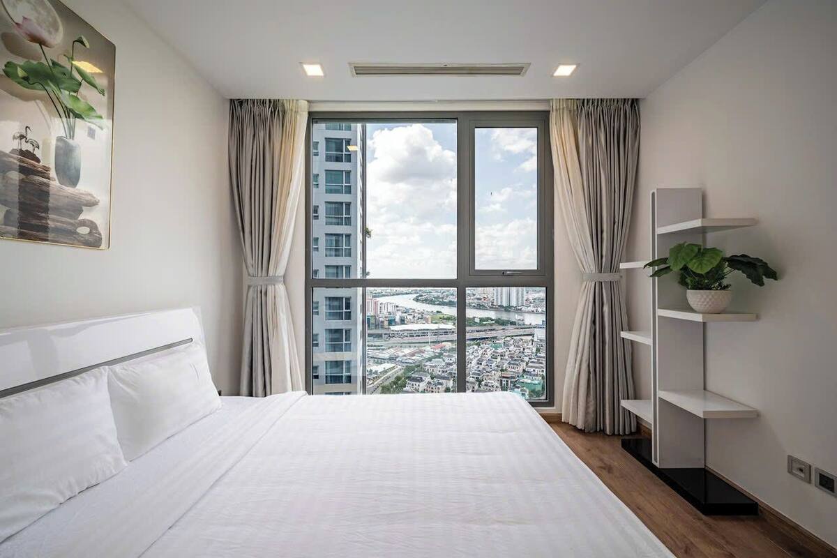 A modern hotel room with a large bed, a view of the cityscape through floor-to-ceiling windows, and a minimalist decor.