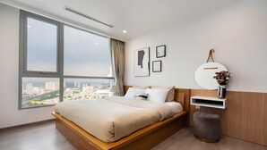 A modern hotel room with a large bed, a city view, a small side table, and a wall-mounted shelf. - YoungC Apartment Landmark (Ho Chi Minh City)